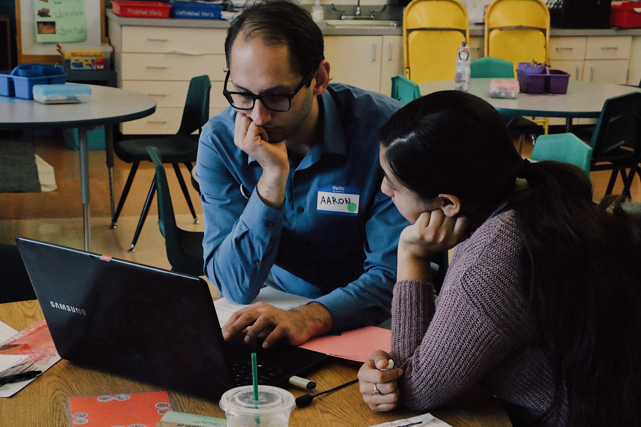 Man and woman sitting at a table huddled around a laptop