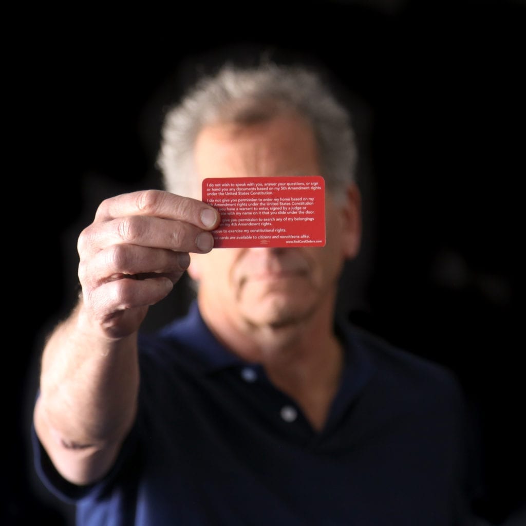 Older man holding a red card in front of his face representing need to Know Your Rights