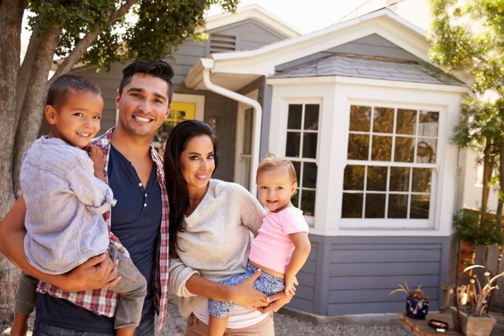 Young Latino family holding two toddlers in front of house