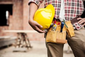 Close-up of construction worker torso, holding construction hat and tools at hip