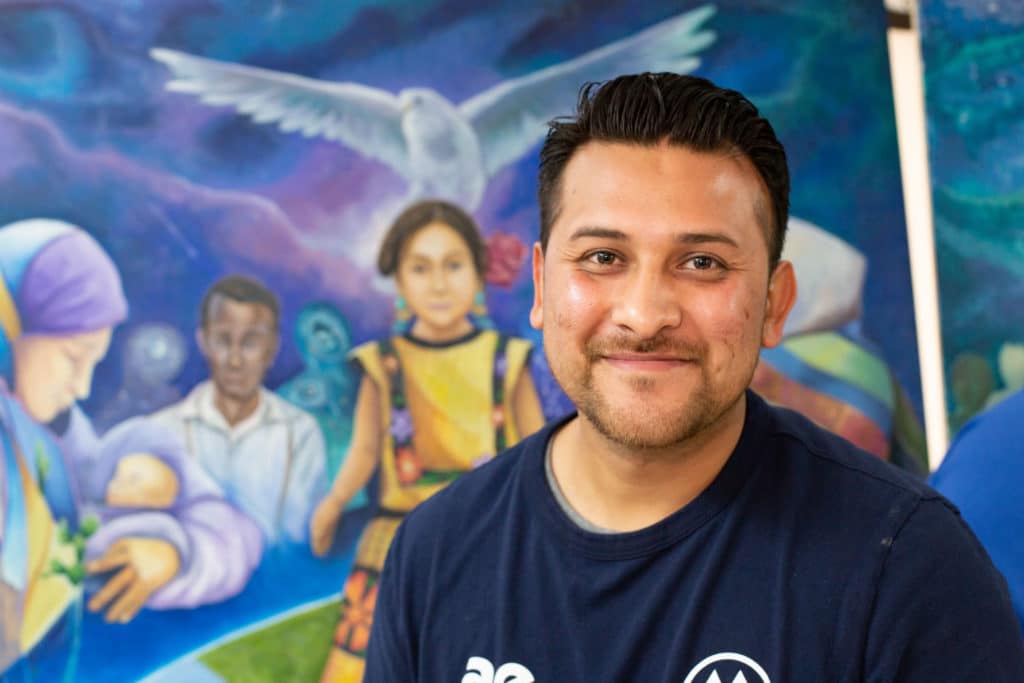 Oscar Morales poses in front of a mural he painted in 2019